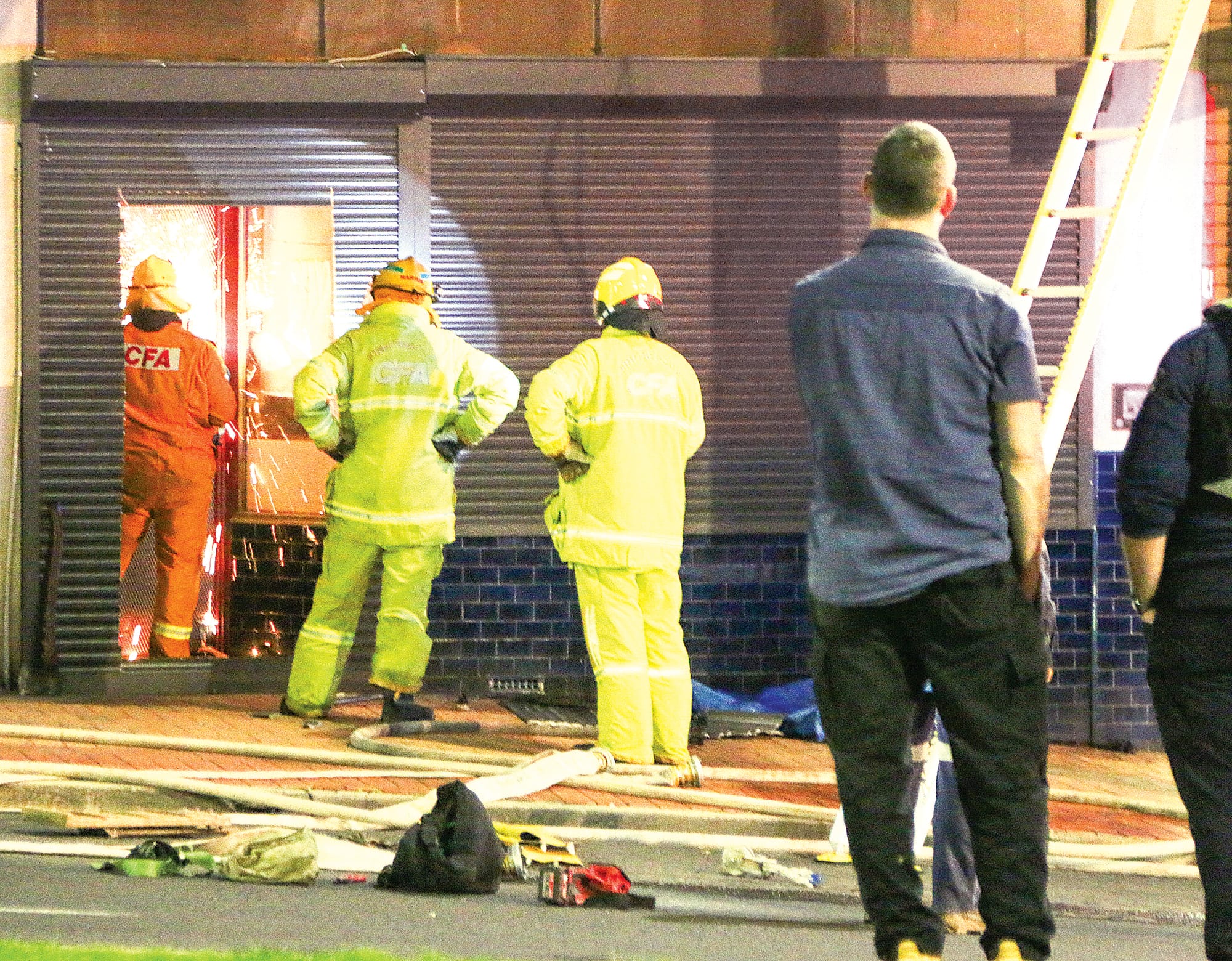 A CFA member cuts through the door of the tobacconist adjoining the Korumburra Newsagency. A12_3022