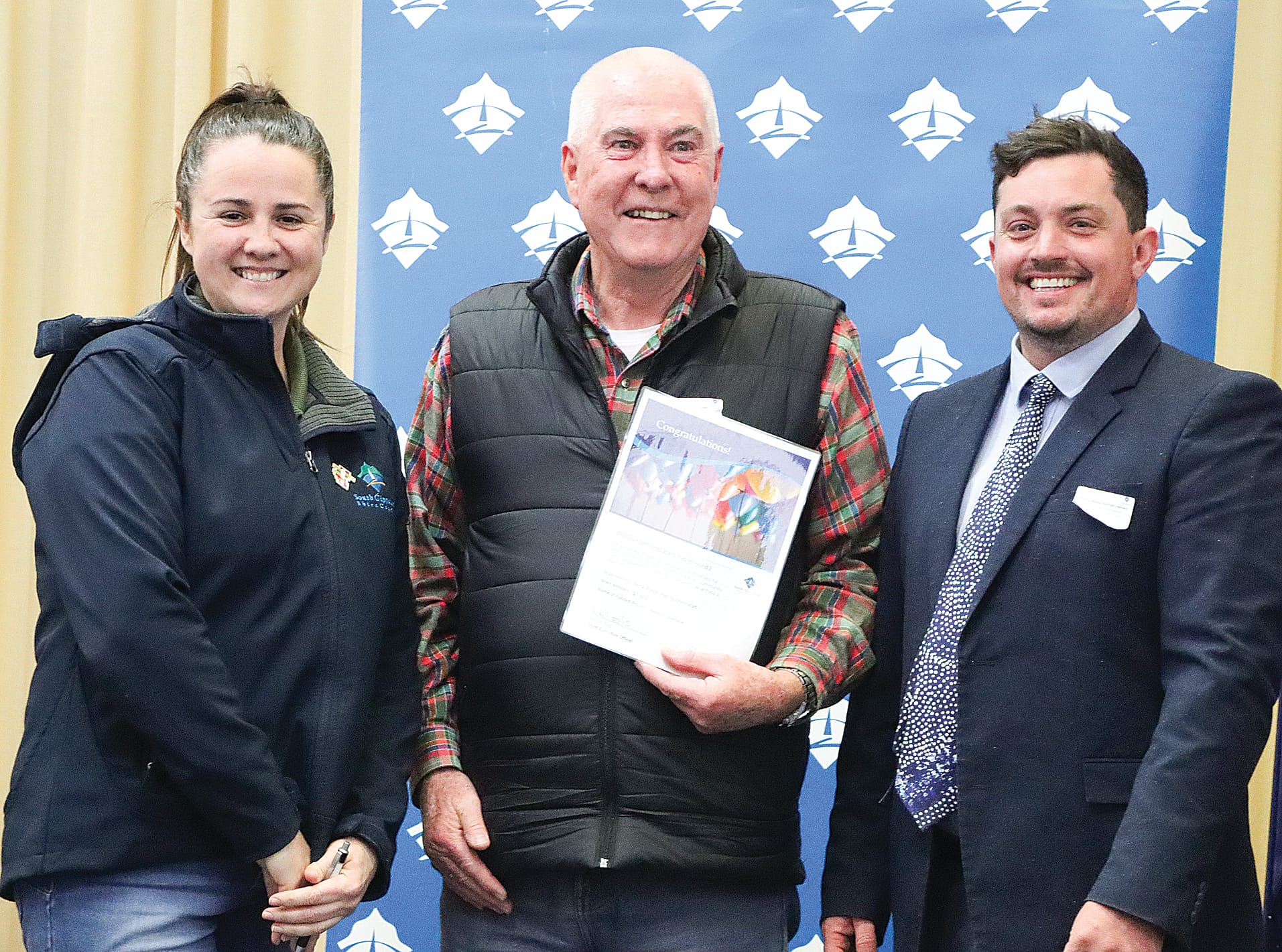 Steve McTaggart receives $1600 on behalf of Bena Public Hall Inc. towards a kitchen air conditioner, with Mayor Clare Williams and Cr Nathan Hersey. A04_3124