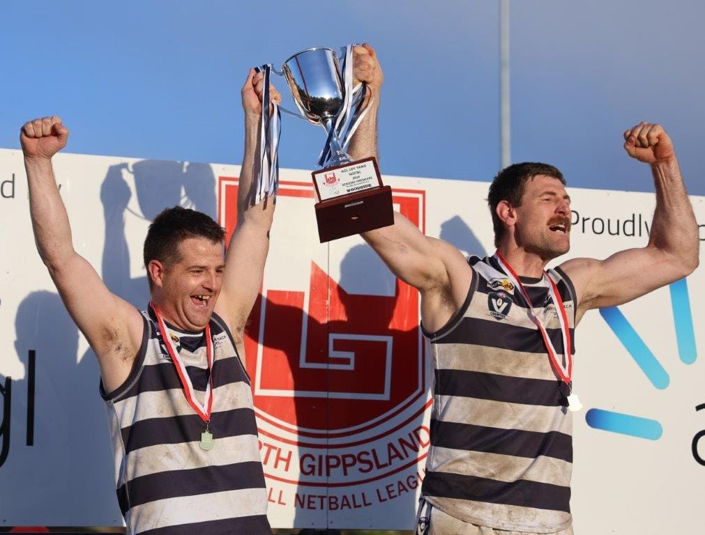 Woodside Wildcats’ coach Mick Stockdale and captain Ryan Foat raise the North Gippsland Senior Premiership Cup after defeating TTU on wintry Saturday at Churchill.