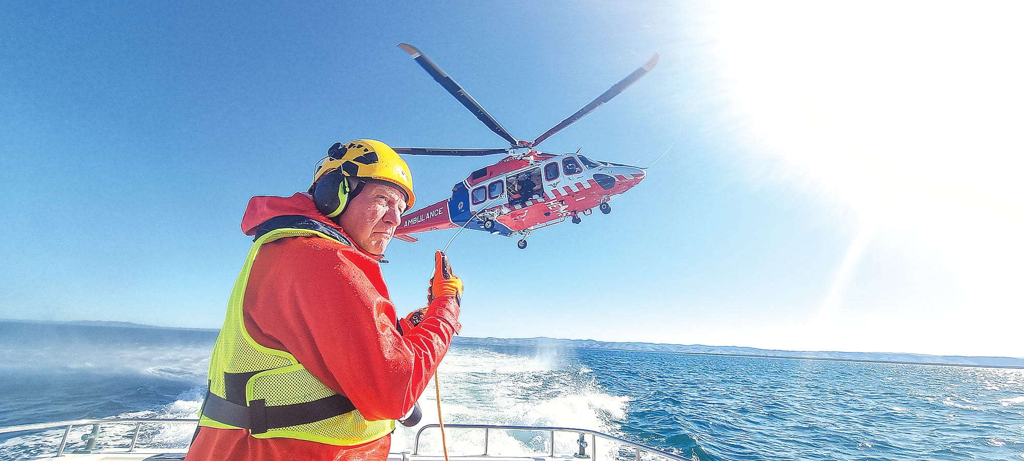 A Port Welshpool Coast Guard crew decked out in full wet weather gear, crash helmet, ear muff, and safety glasses handles the Victorian Air Ambulance Helimed rescue chopper overhead that has dropped a fender line to the deck. Photo Jonathon Stevenson