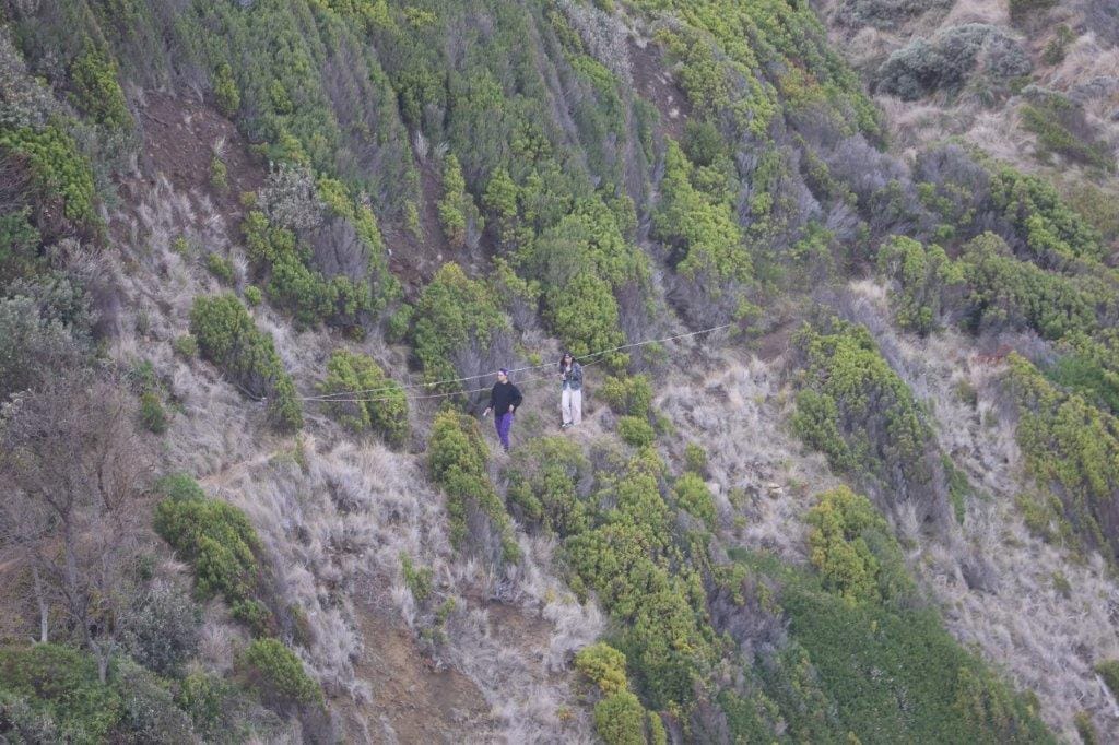 Visitors to Punch Bowl Rocks scale the narrow track leading down the cliff to the rocks with a small dog leading the way.