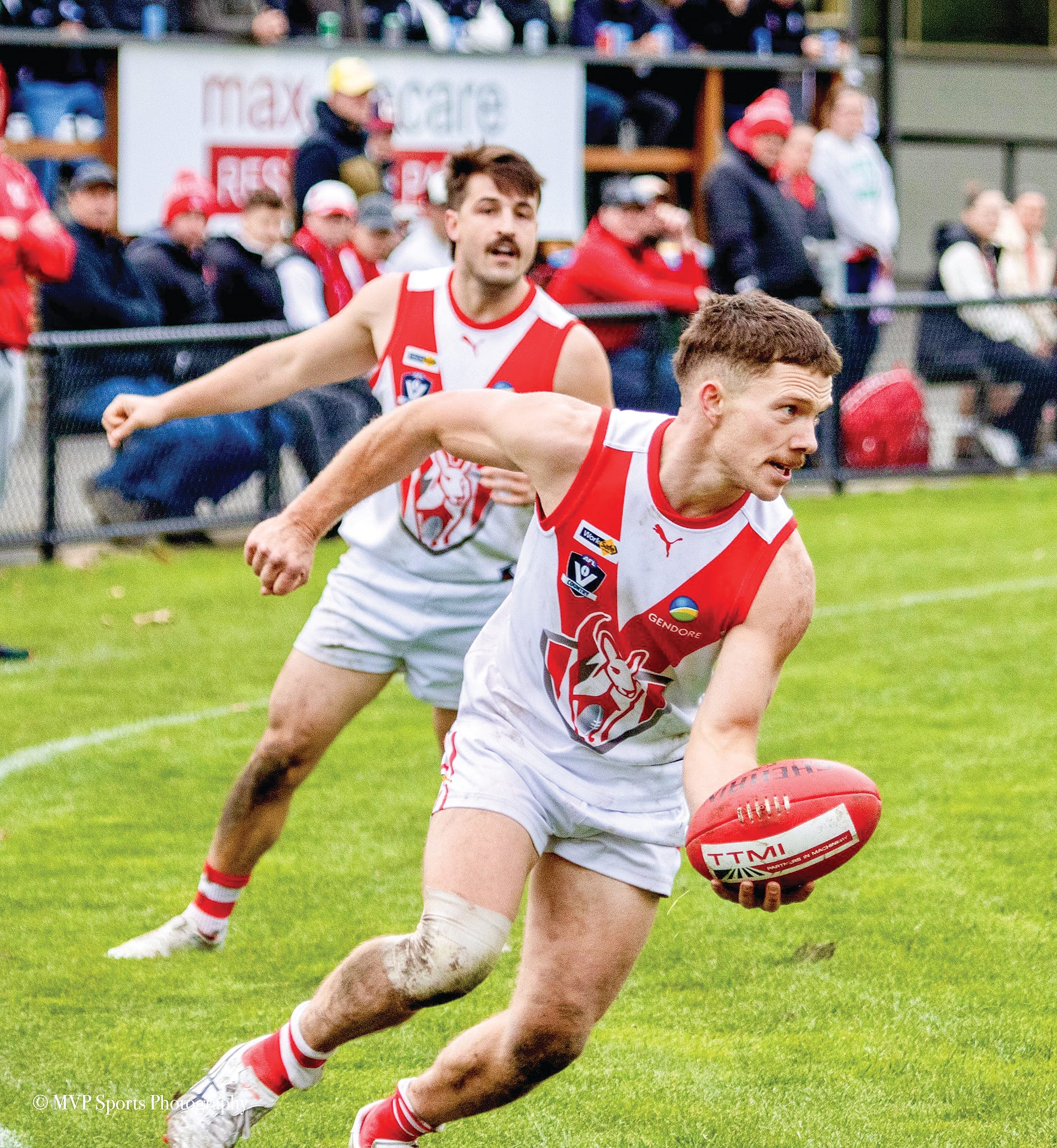 Harry Sith looks to handball off the Sherrin whilst Timm Gavenlock looks on from behind in support.