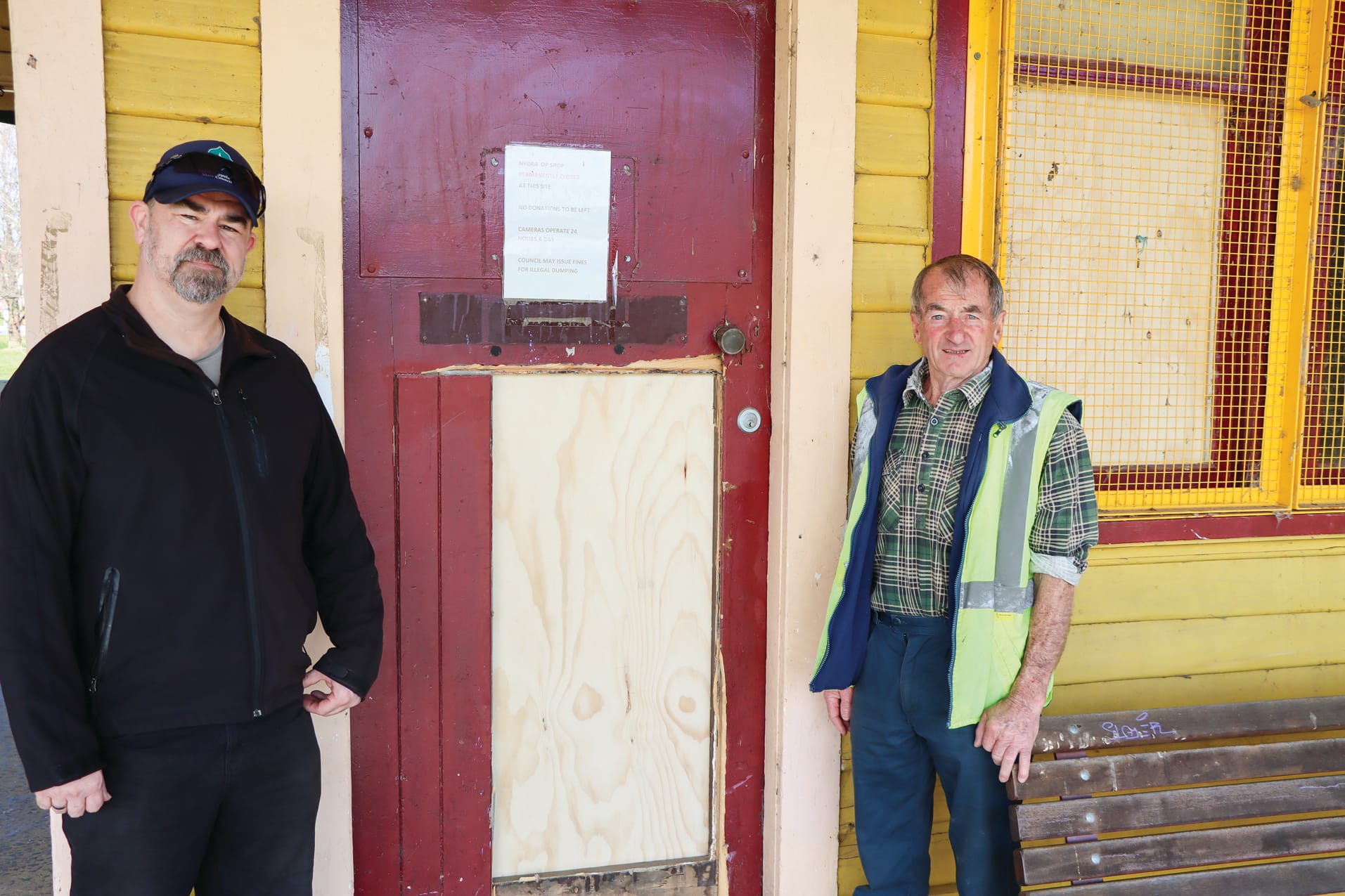 Mick Felton and Gilbert Kelly stand near the damaged door and one of the vandalised windows at Nyora Railway Station.