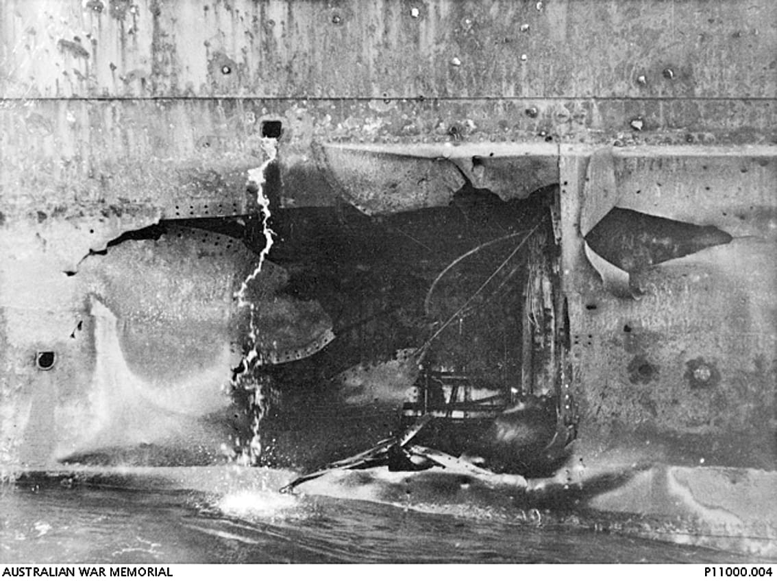 A 12-foot by 14-foot hole on the waterline under the bridge on the port side of HMAS Australia. This damage was inflicted by a Japanese Kamikaze aircraft attack on 7 January 1945. A temporary patch is covering the damage. Photo: Australian War Memorial Collection.